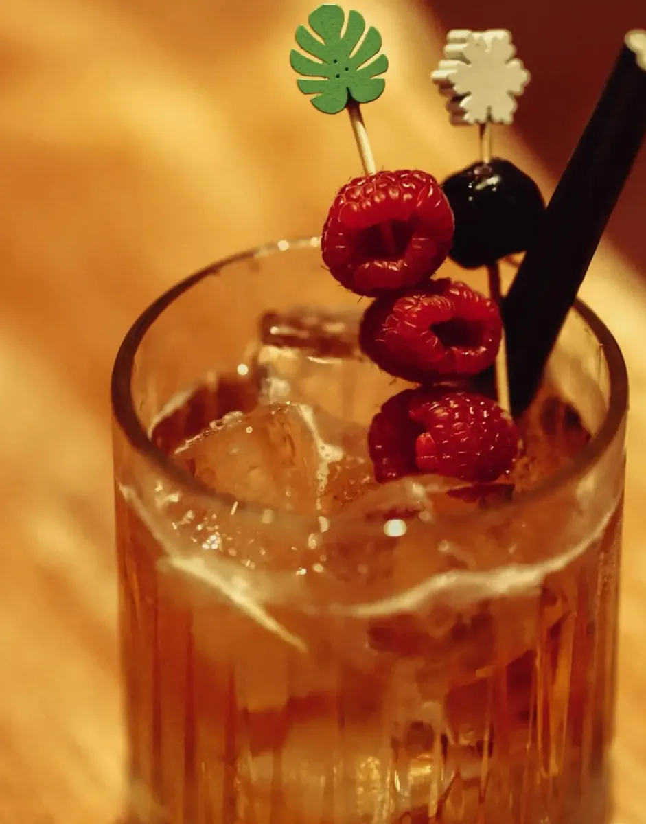 Amber cocktail with raspberries on a pick