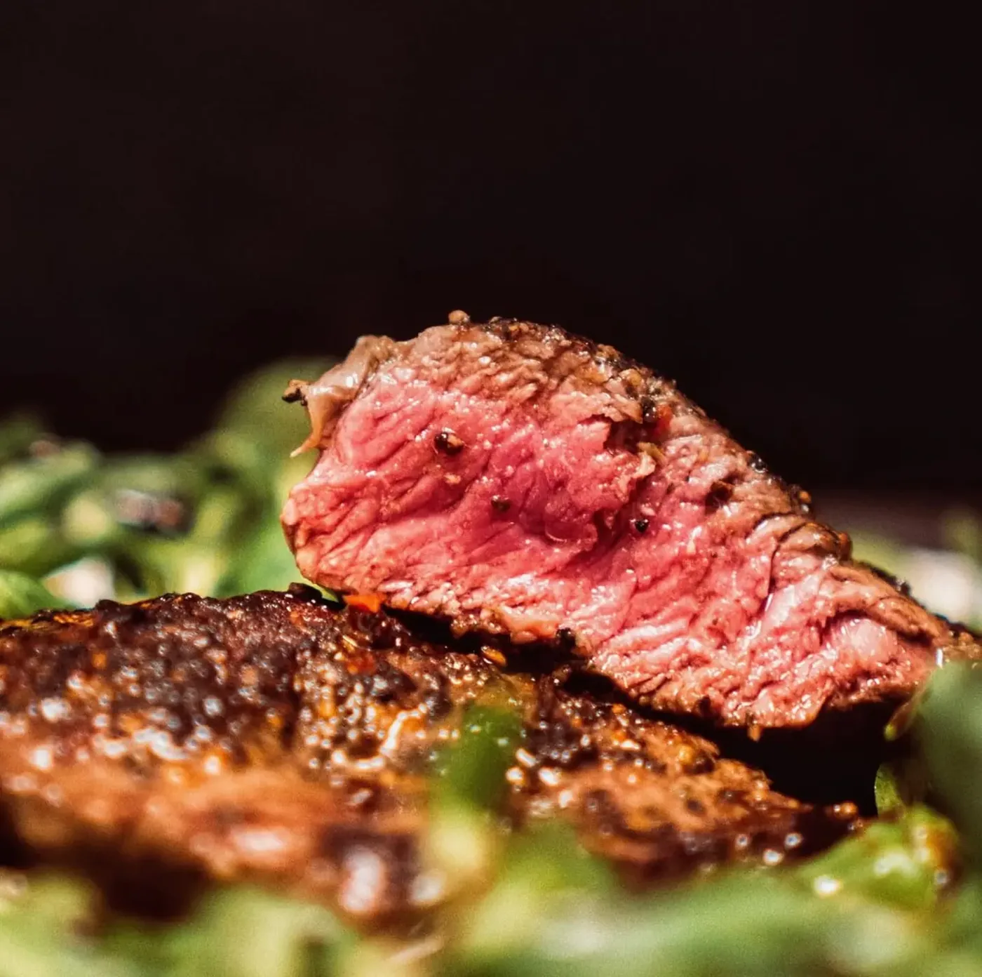 Sliced steak seasoned with cracked pepper over salad leaves